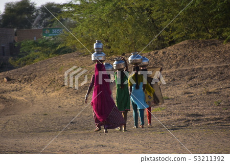 莎麗服的美麗的婦女在民間服裝，Cooley村莊，Jaisalmer，印度運載井水的圖在他們的頭 53211392