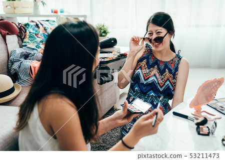smiling girl friends putting makeup on together 53211473