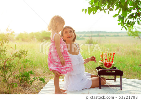 Two smiling girls eats slice of watermelon outdoors on meadow. Mother and daughter spend time 53221798