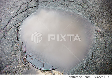 The puddle on the manhole in asphalt surface 53224103