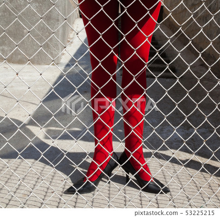 Woman's legs in red tights behind the metal mesh Woman's legs in red tights behind the metal mesh 53225215