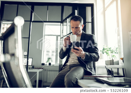 Businessman having coffee break and reading message on phone Businessman having coffee break and reading message on phone 53226109