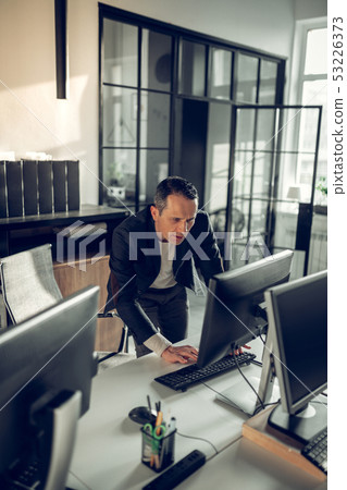 Mature dark-haired businessman checking his e-mail on computer Mature dark-haired businessman checking his e-mail on computer 53226373