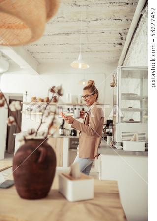 Smiling woman answering her messages and drinking coffee. 53227452