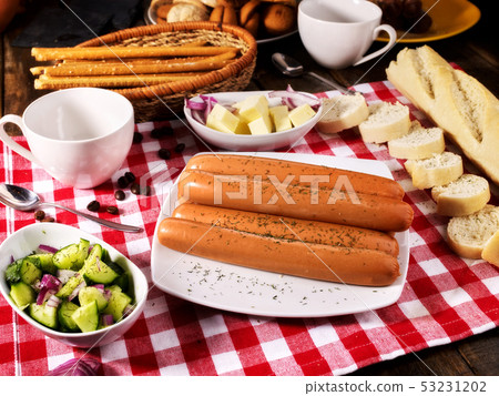 Sausage portion with baguette on table setting on checkered cloth 53231202