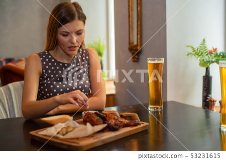 Beautiful girl eats chicken leg with beer in restaurant 53231615