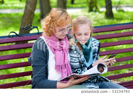 mom and daughter read a magazine in the park mom and daughter read a magazine in the park 53234793