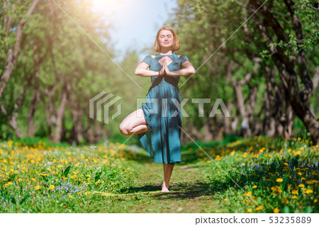 Photo of woman with closed eyes in long green dress doing yoga in forest Photo of woman with closed eyes in long green dress doing yoga in forest 53235889