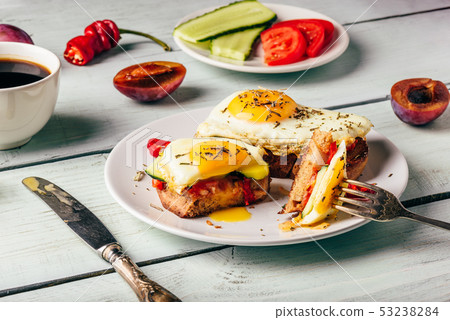 Bruschettas with vegetables and fried egg, cup of coffee and som 53238284