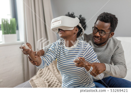 African couple play video games wearing virtual reality glasses at home 53269421