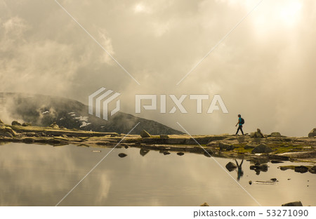 Silhouette of backpacker walking towards the edge of rocky lake. Norway Silhouette of backpacker walking towards the edge of rocky lake. Norway 53271090