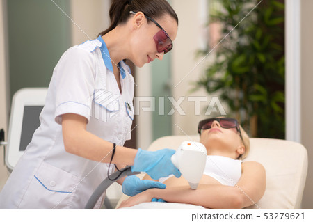 Dark-haired master wearing uniform doing laser depilation on arms 53279621