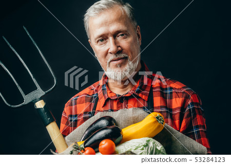 old garderner is holding vegetables and pitchfork old garderner is holding vegetables and pitchfork 53284123