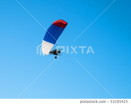 Colorful powered paraglider against blue sky. 53285425
