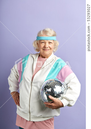 Happy senior woman in white sportswear holding discoball in hands on purple Happy senior woman in white sportswear holding discoball in hands on purple 53293027