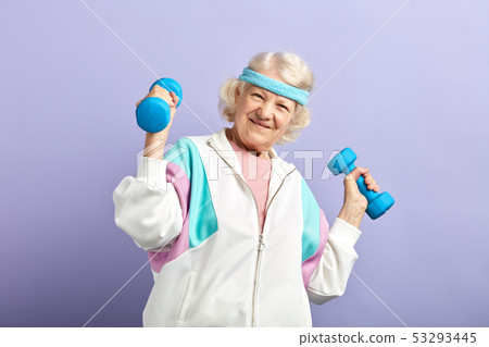 Cheerful elderly woman exercising with a pair of dumbbells and smiling Cheerful elderly woman exercising with a pair of dumbbells and smiling 53293445