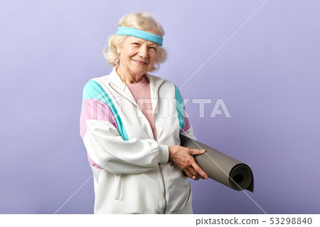 Happy female pensioner holding yoga mat in hands, comes to yoga class in studio 53298840
