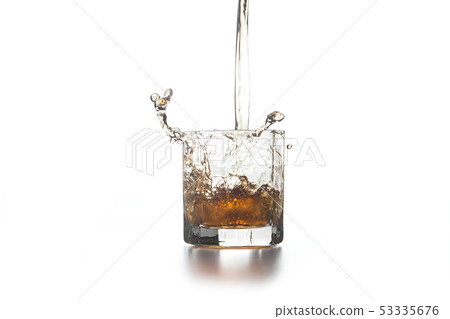 Whiskey pouring into glass with ice on light 53335676
