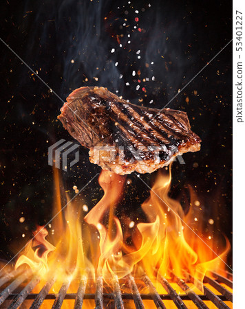 Tasty beef steaks flying above cast iron grate with fire flames. 53401227
