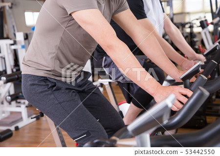Men riding a bicycle in a gym Men riding a bicycle in a gym 53442550