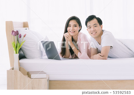 Asian couple lie prone on bed in bedroom.. 53592583