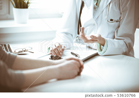 Doctor and female patient sitting at the desk and talking in clinic near window. Medicine and health Doctor and female patient sitting at the desk and talking in clinic near window. Medicine and health 53610766
