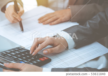 Two female accountants counting on calculator income for tax form completion hands close-up Two female accountants counting on calculator income for tax form completion hands close-up 53611840