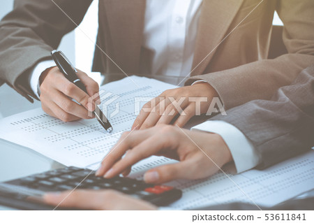 Two female accountants counting on calculator income for tax form completion hands close-up Two female accountants counting on calculator income for tax form completion hands close-up 53611841