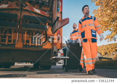Two refuse collection workers loading garbage into waste truck Two refuse collection workers loading garbage into waste truck 53612144