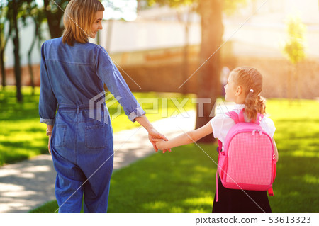 Parent and pupil of primary school go hand in hand. Woman and girl with backpack behind the back 53613323