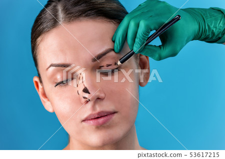 Beautician draw correction lines on woman face. Before plastic surgery operetion. Isolated on blue Beautician draw correction lines on woman face. Before plastic surgery operetion. Isolated on blue 53617215