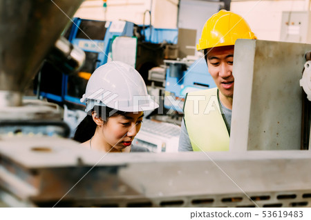 Young Asian male factory worker teaching Asian female apprentice Young Asian male factory worker teaching Asian female apprentice 53619483