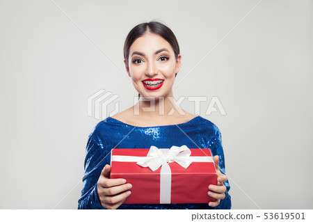Happy young woman in braces holding red gift box Happy young woman in braces holding red gift box 53619501