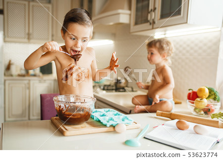 Little kids tastes melted chocolate on the kitchen 53623774