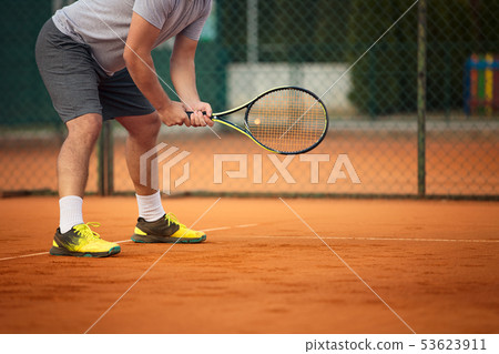 Close up of man holding tennis racket on clay court. On court is sunset. Man holding tennis racket Close up of man holding tennis racket on clay court. On court is sunset. Man holding tennis racket 53623911