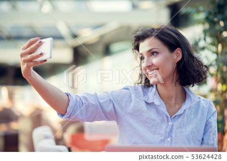 Portrait of a playful young girl taking selfie with mobile phone while sitting with laptop computer 53624428
