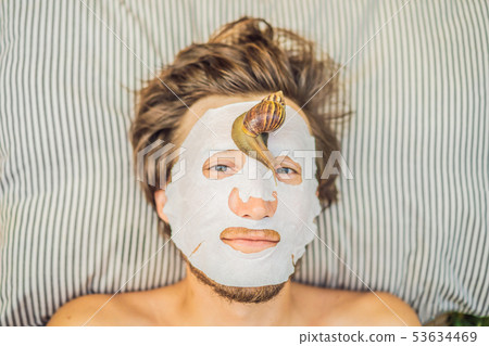 Young man makes a face mask with snail mucus. Snail crawling on a face mask. SPA for man, SPA for Young man makes a face mask with snail mucus. Snail crawling on a face mask. SPA for man, SPA for 53634469