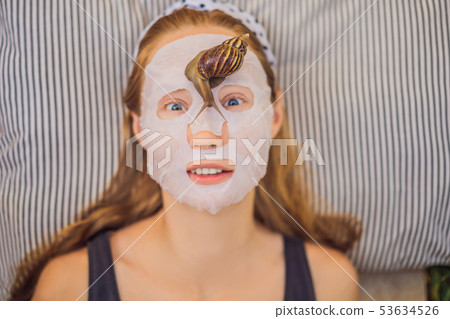 Young woman makes a face mask with snail mucus. Snail crawling on a face mask Young woman makes a face mask with snail mucus. Snail crawling on a face mask 53634526