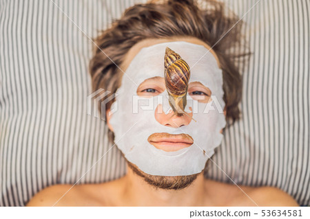 Young man makes a face mask with snail mucus. Snail crawling on a face mask. SPA for man, SPA for Young man makes a face mask with snail mucus. Snail crawling on a face mask. SPA for man, SPA for 53634581
