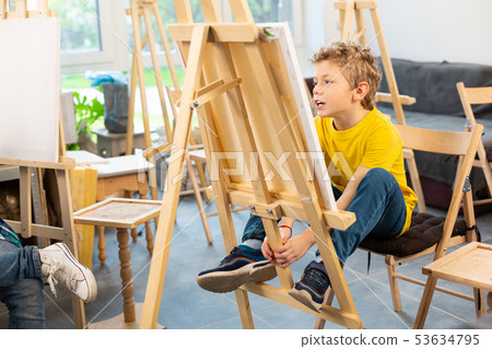 Schoolboy sitting near painting easel in art school 53634795