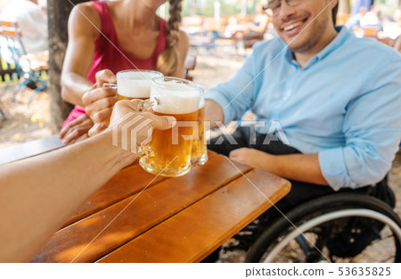 Friends in beer garden drinking, one man is in a wheelchair  53635825