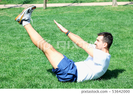fitness man exercising sit up outside in grass in fitness man exercising sit up outside in grass in 53642000