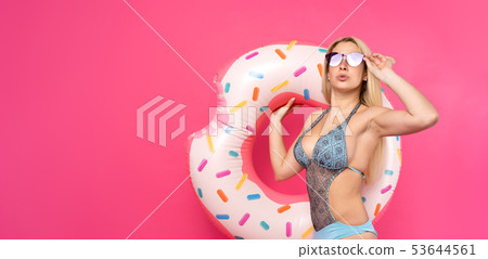 Image of blonde in bathing suit with inflatable donut on empty pink background in studio Image of blonde in bathing suit with inflatable donut on empty pink background in studio 53644561