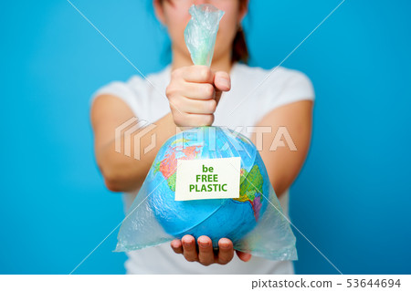 Woman holds in hands plastic bag with sticker text be FREE PLASTIC and planet earth at blue 53644694