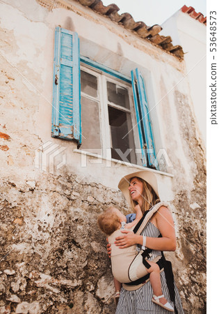 A young mother with a baby in a carrier walking in town on summer holiday. A young mother with a baby in a carrier walking in town on summer holiday. 53648573