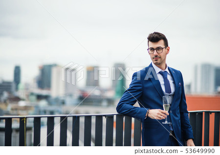 A young businessman with glass on a party outdoors on roof terrace in city. A young businessman with glass on a party outdoors on roof terrace in city. 53649990