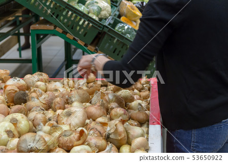 the girl chooses onions on a counter of shop 53650922