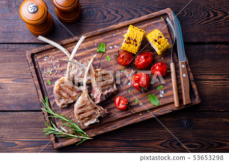 Lamb ribs grilled on cutting board with roasted vegetables. Top view. Lamb ribs grilled on cutting board with roasted vegetables. Top view. 53653298