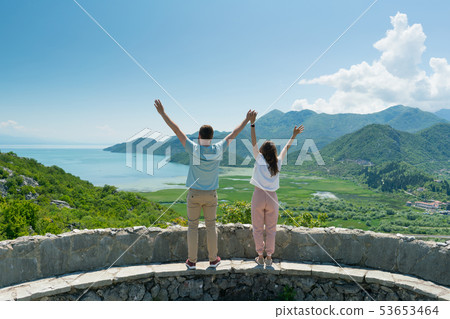 couple on a viewing platform enjoying the view of the lake and mountains on a sunny day 53653464
