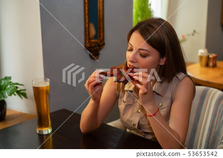 Beautiful girl eats chicken leg with beer in restaurant Beautiful girl eats chicken leg with beer in restaurant 53653542